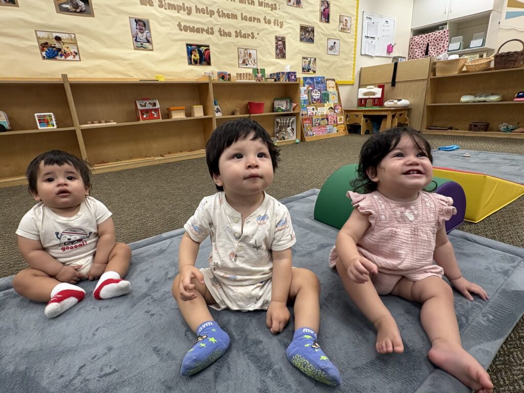 Three infants sitting together on a soft mat in the infant classroom